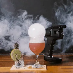 Pistolet à bulles noir près d'un cocktail rosé coiffé d'une bulle de fumée parfumée