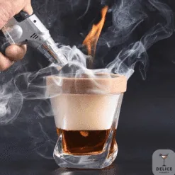 Verre à whisky ambré fumé recouvert d'un couvercle en bois, flambé au chalumeau, fond noir Délice Bar