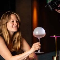 Femme tenant un cocktail rosé surmonté d'une bulle de fumée formée par le Flavour Blaster Pro 2.4