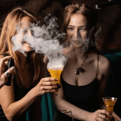 Deux femmes dans un bar tenant des verres cornet à cocktail dégageant de la fumée aromatique