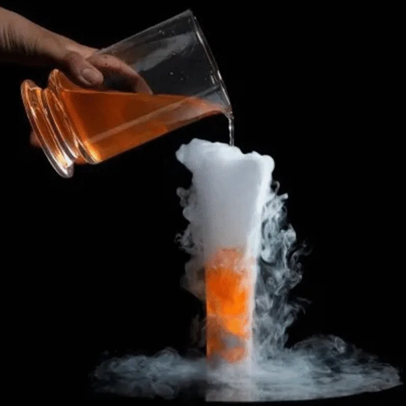 Cocktail orange versé dans un verre conique débordant de fumée blanche de glace carbonique