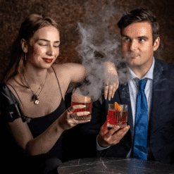 Couple trinquant avec deux cocktails fumants aux arômes parfumés dans une ambiance feutrée