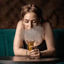 Femme inhalant la fumée neutre s'échappant d'un cocktail dans un verre coupe