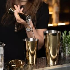 Barmaid versant au jigger dore dans les timbales Boston Fusion dorees, passoire et romarin sur le bar