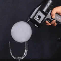 Pistolet a bulles deposant une grosse bulle de fumee blanche au-dessus d'un verre a pied