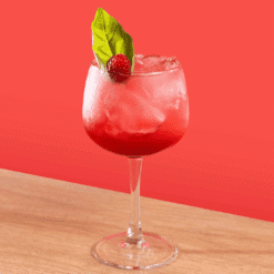 Cocktail rouge framboise dans un verre à pied garni de basilic et d'une framboise fraîche sur fond rouge
