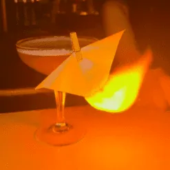 Papier flash blanc plié posé sur verre à cocktail dans une ambiance de bar chaleureuse orangée