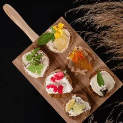 Wooden board of gourmet canapés topped with colourful lemon, strawberry and citrus pearls