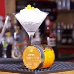 Martini glass filled with crushed ice topped with orange citrus pearls, Zitron naranja jar at the bar