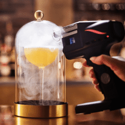 Cocktail jaune sous cloche en verre à socle doré rempli de fumée par un pistolet