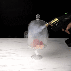 Pistolet à fumée remplissant une cloche en verre sur présentoir au-dessus d'un dessert