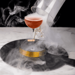 Cocktail rouge fumé sous cloche en verre sur socle doré entouré de fumée épaisse