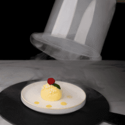 Cloche en verre levée libérant la fumée au-dessus d'un dessert citronné garni de baie rouge