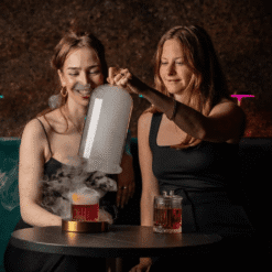 Femme versant de la fumée d'une cloche en verre dans un cocktail en bar tamisé