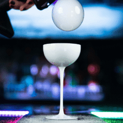 Bulle savonneuse en lévitation au-dessus d'un verre coupe blanc à pied dans un bar lumineux