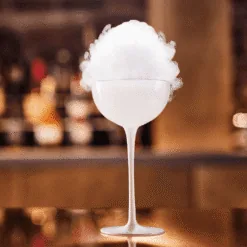 Verre coupe blanc à pied couronné d'un nuage de barbe à papa blanche pour cocktail spectaculaire au bar