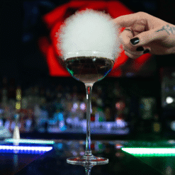 Verre à bulle coupe garni d'une boule de barbe à papa nuageuse au-dessus d'un cocktail au bar