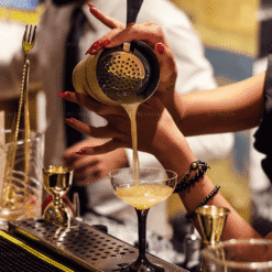 Barman filtrant un cocktail doré au travers d'une passoire dans un verre à martini au bar