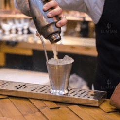 Barman versant un cocktail mousseux du shaker cobbler Kenta inox dans un verre métallique