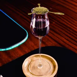 Support de bulle doré posé sur un verre à pied contenant un cocktail violet au bar