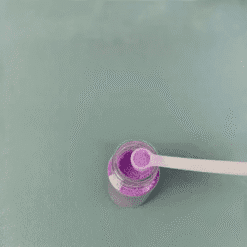 Pot de paillettes comestibles violettes ouvert avec cuillère doseuse blanche pour cocktails scintillants