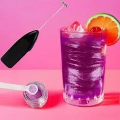 Cocktail violet pailleté scintillant garni d'orange et cerise, avec mousseur noir et pot de paillettes comestibles