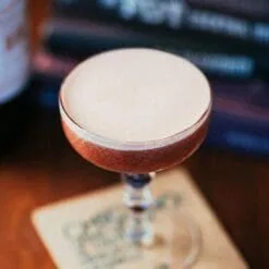 Cocktail mousseux crémeux dans verre coupe posé sur un sous-verre, ambiance feutrée