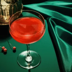Coupe de cocktail rouge translucide sur fond de satin vert émeraude, paillettes comestibles rouges pour cocktails
