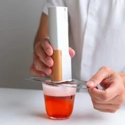 Main utilisant le stylo imprimante alimentaire Evebot avec pochoir sur cocktail rose mousseux
