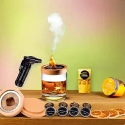 Fumoir à cocktail en bois et cuivre avec verre whisky fumé, chalumeau noir, copeaux cherry et tranches d'orange