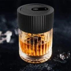 Fumoir electrique noir pose sur verre de whisky ambre fume, ambiance sombre avec glaçons
