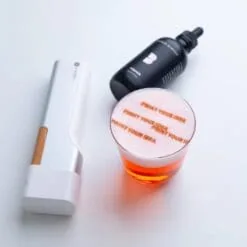 Penna stampante alimentare bianca e flacone d'inchiostro nero che stampa Print Your Idea sulla schiuma di un cocktail arancione