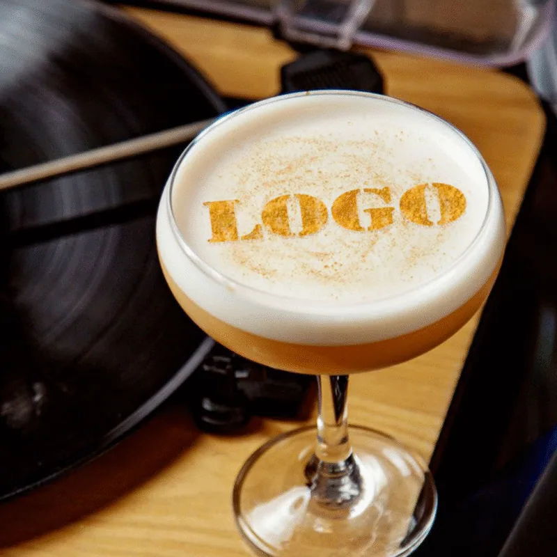 Cocktail coupe à mousse blanche imprimée du mot LOGO doré devant une platine vinyle