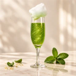 Champagne flute with a sparkling green cocktail, topped with candyfloss and served with mint.