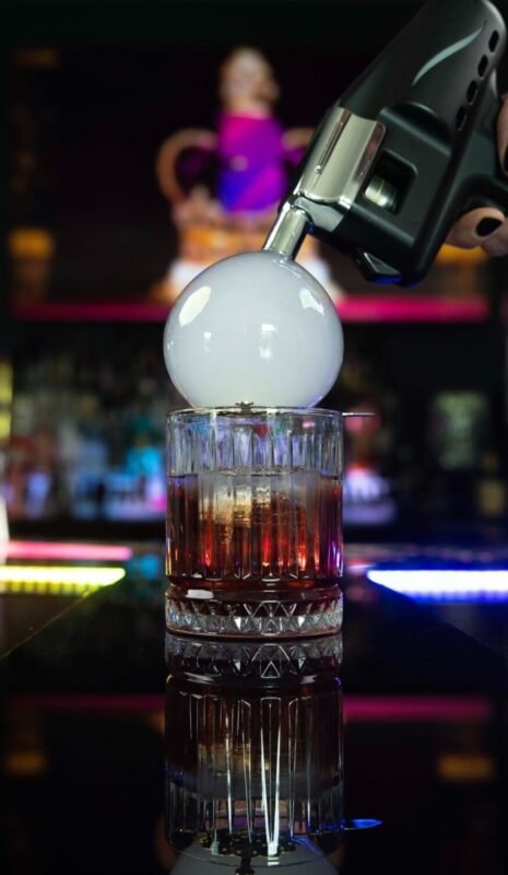 Pistola a bolle che deposita una grande bolla di fumo su un cocktail ambrato